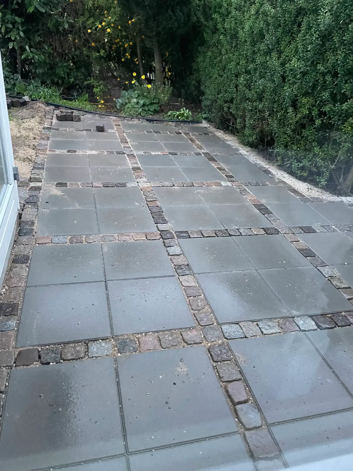 Færdig fliseterrasse med brostens-grid og havemøbler